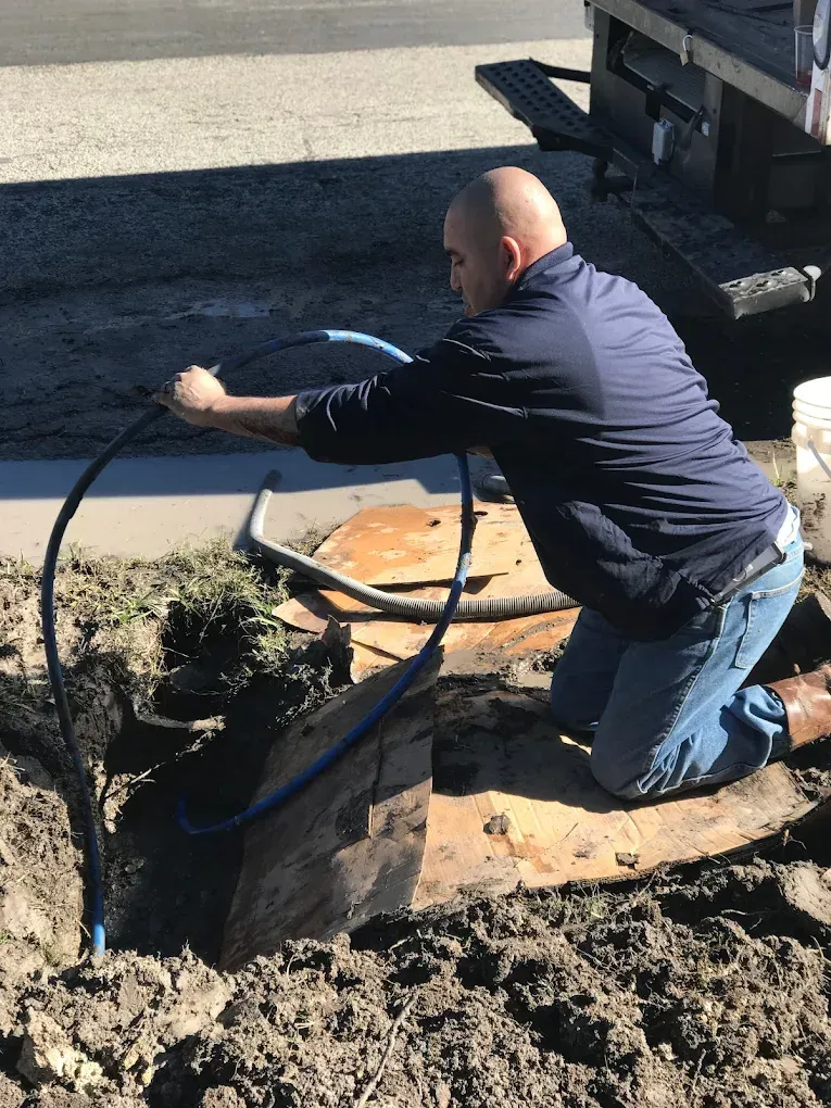 A man is kneeling down in the dirt holding a hose.
