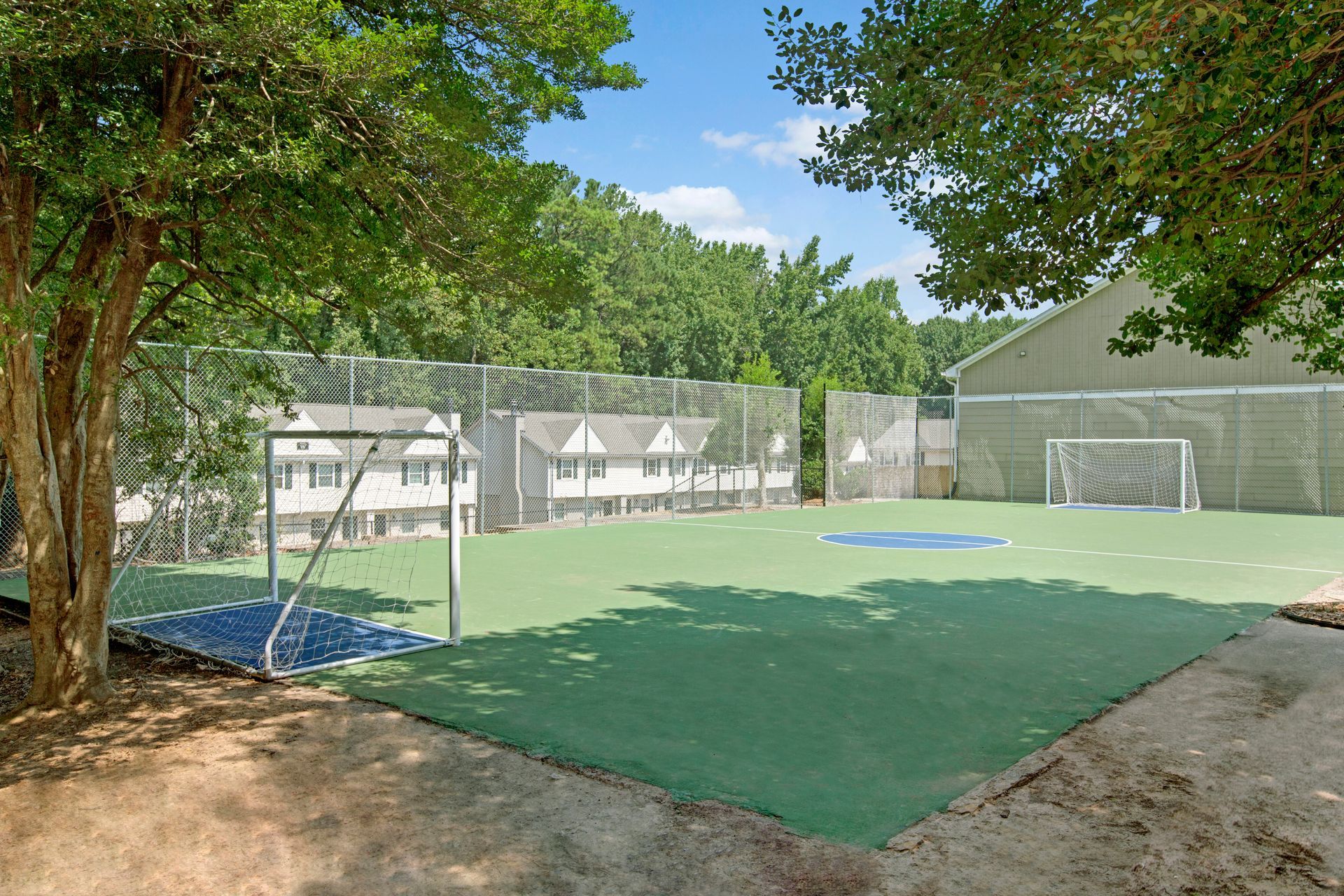 Soccer field with goals, green turf, and fence in front of townhouses, under blue sky.