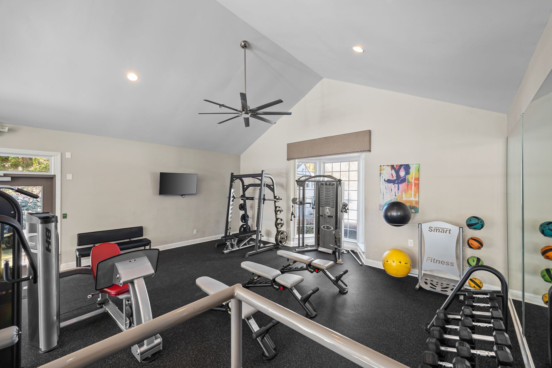 Gym with various exercise equipment, dark floor, neutral walls, and a ceiling fan.