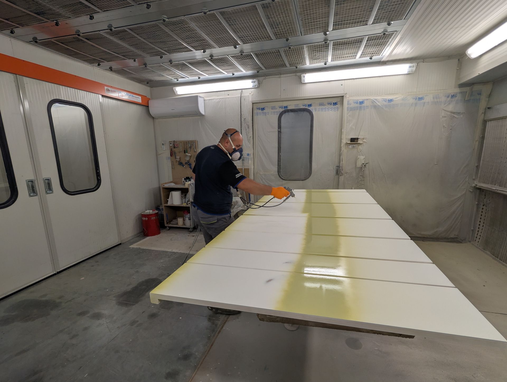 Un uomo sta dipingendo un pezzo di legno in una cabina di verniciatura.