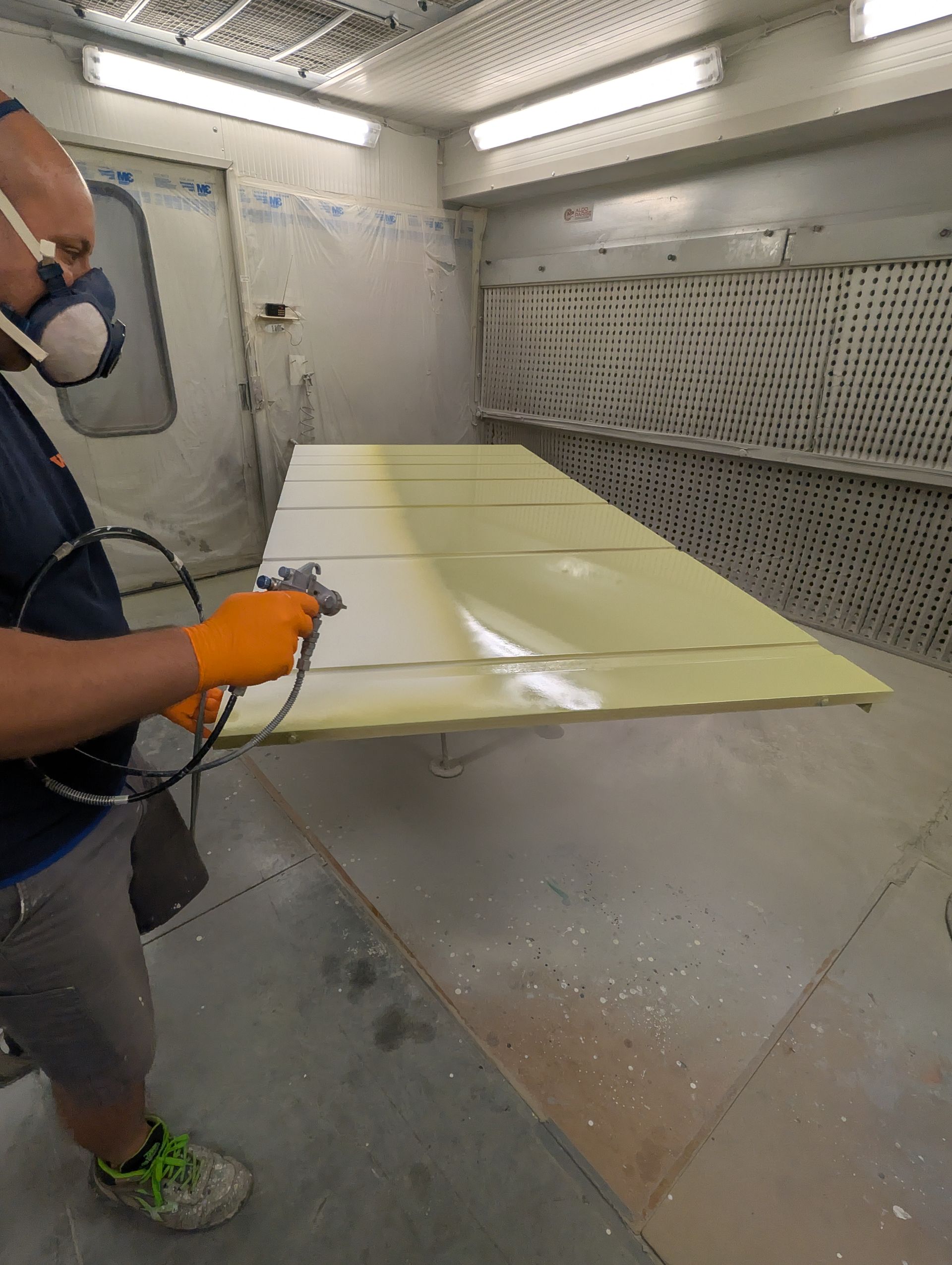 Un uomo sta verniciando a spruzzo un pezzo di legno in una cabina di verniciatura.
