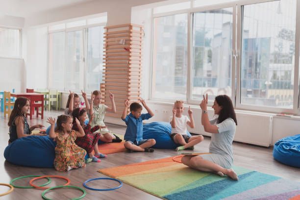 A happy teacher sitting and playing hand games with a group of children in a childcare center.