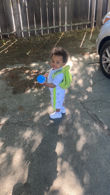 A little boy is standing on the sidewalk holding a blue toy.
