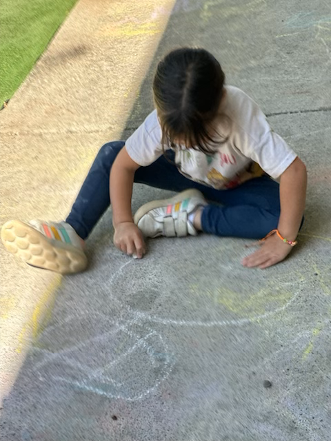 A little girl is sitting on the ground drawing with chalk