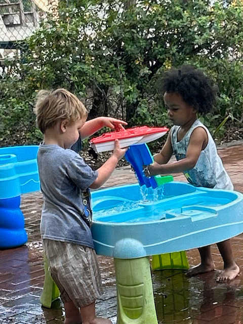 Two young children are playing with a water table.