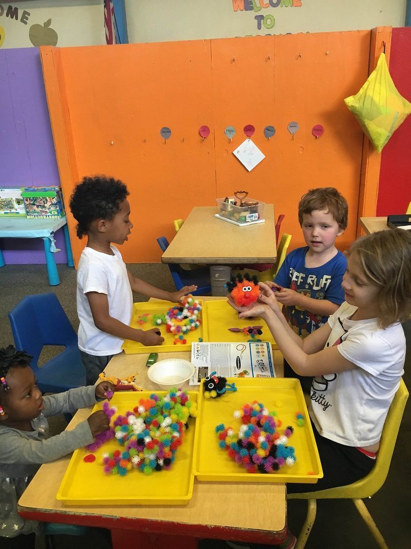 A group of children are playing with pom poms at a table.