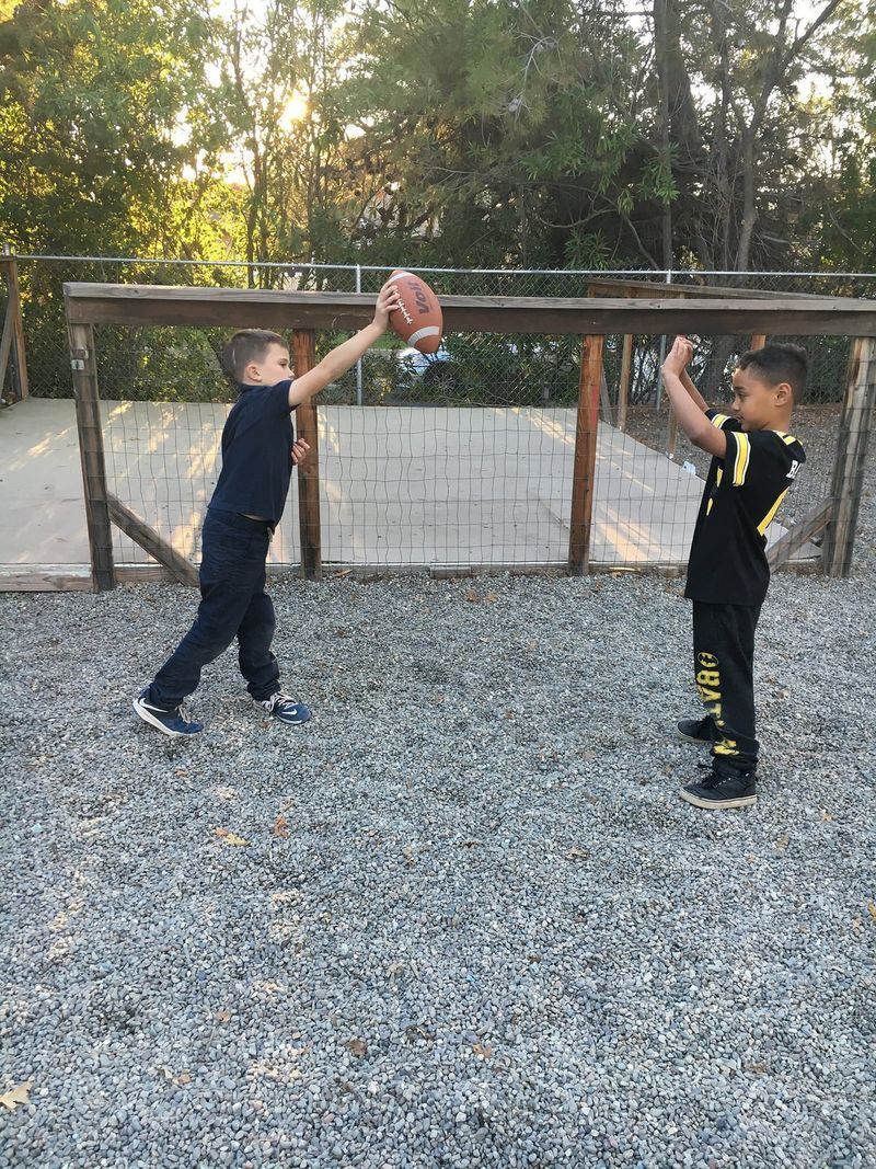 Two young boys are playing with a ball in a gravel area.
