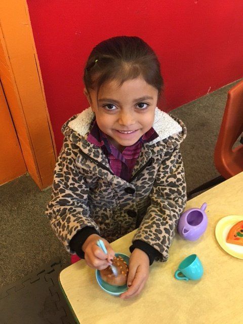 A little girl is sitting at a table playing with a tea set