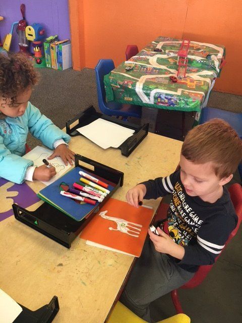 A boy and a girl are sitting at a table playing with markers