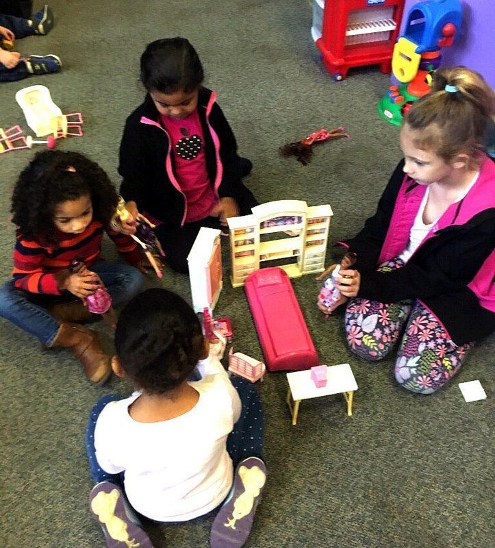 A group of young girls are sitting on the floor playing with toys