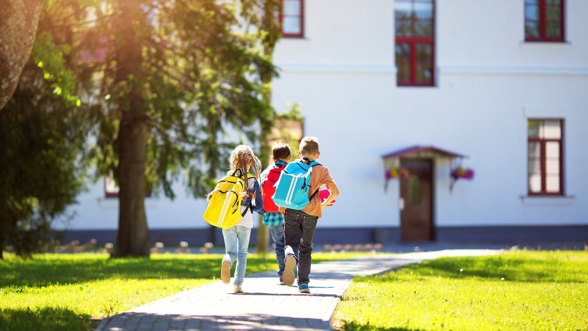 A group of children are walking down a sidewalk towards a school building.