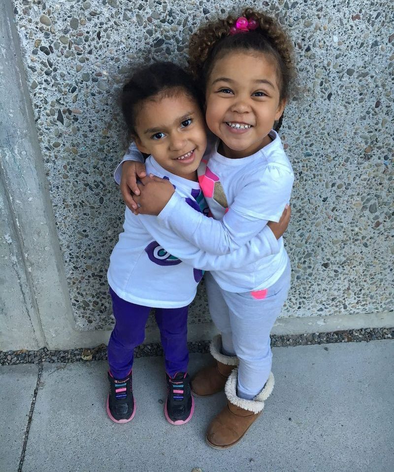 Two little girls hugging each other in front of a wall