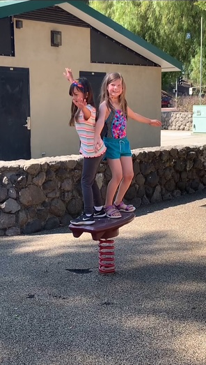 Two young girls are playing on a seesaw in a park.