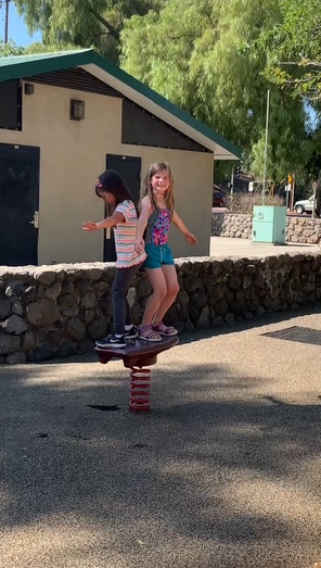 Two young girls are playing on a seesaw in a park.