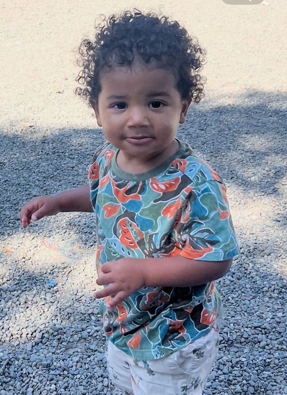 A little boy is standing on the sidewalk holding a blue toy.