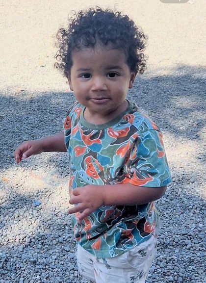 A little boy is standing on the sidewalk holding a blue toy.