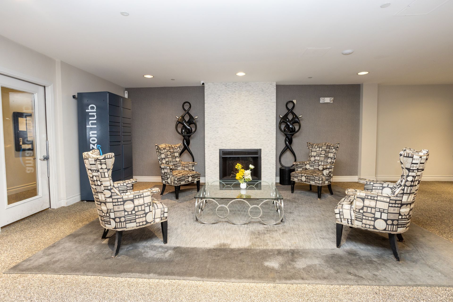 Lounge area with patterned armchairs around a fireplace, floral arrangement, and Amazon Hub lockers.