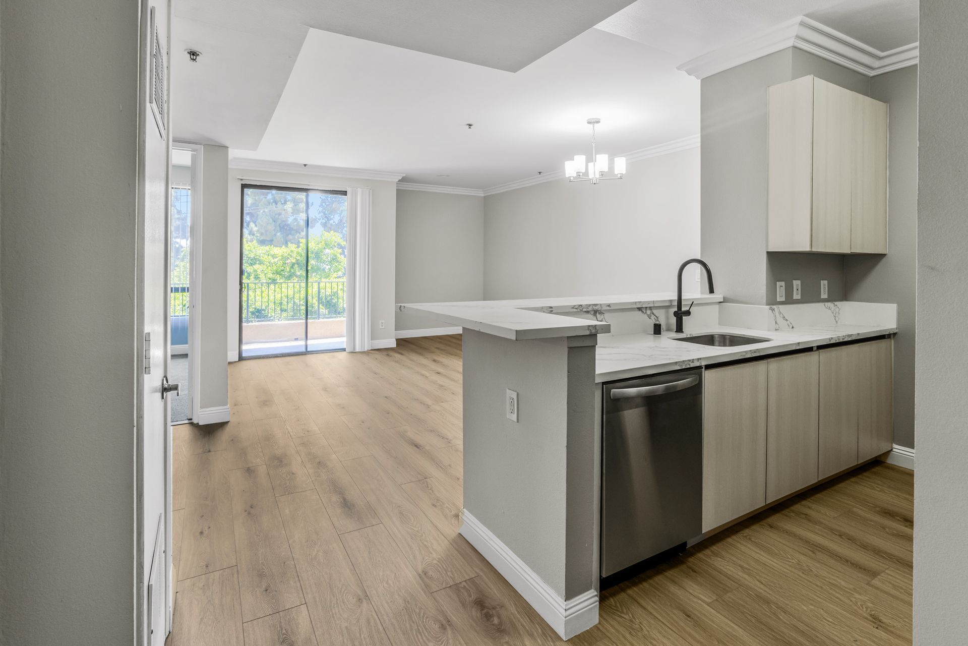 Modern kitchen with light wood floor, white countertops, stainless steel appliances, and a balcony.