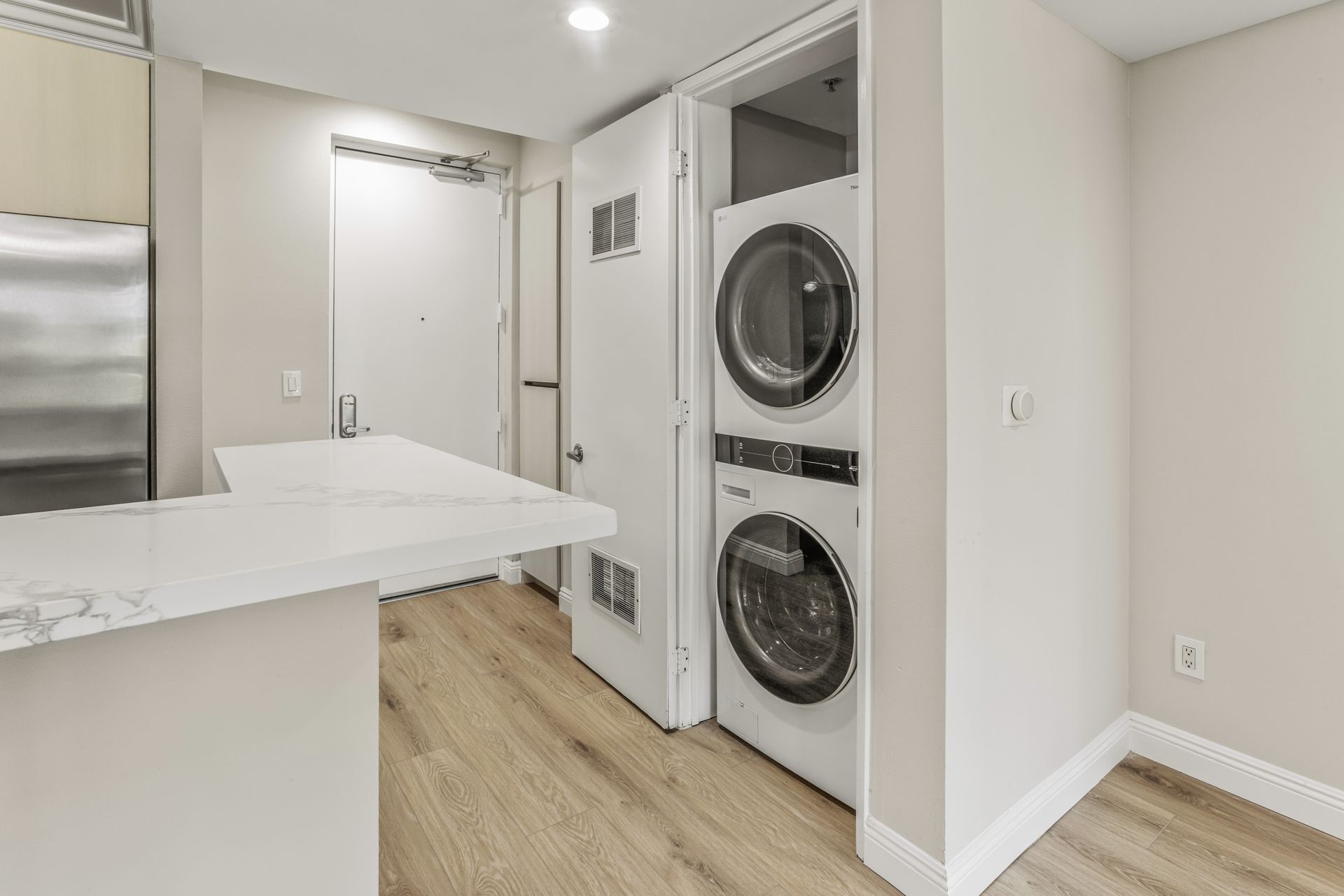 Laundry machines stacked in a white closet next to a white countertop and hardwood floor.