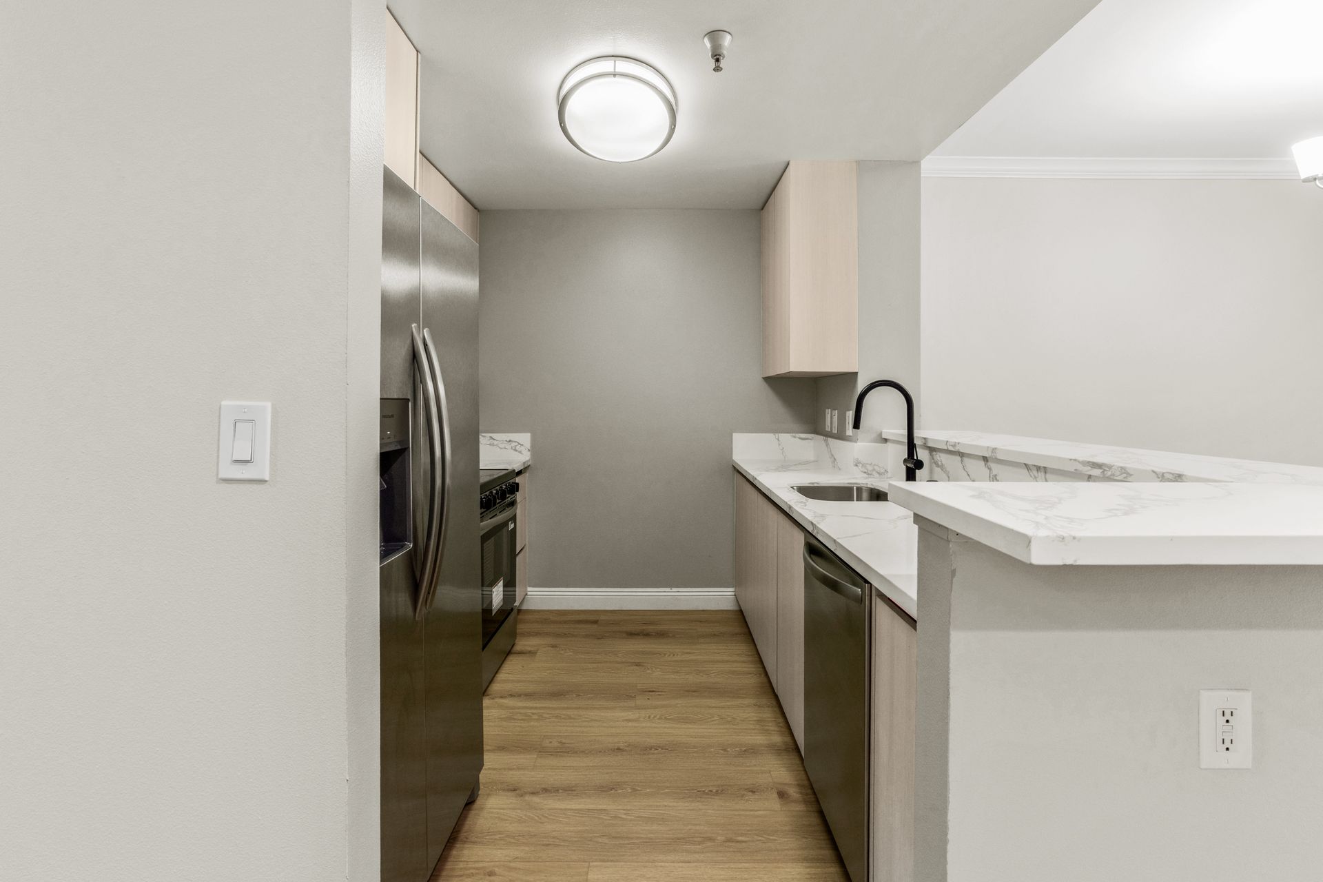Modern kitchen with stainless steel appliances, light wood floors, and white countertops.