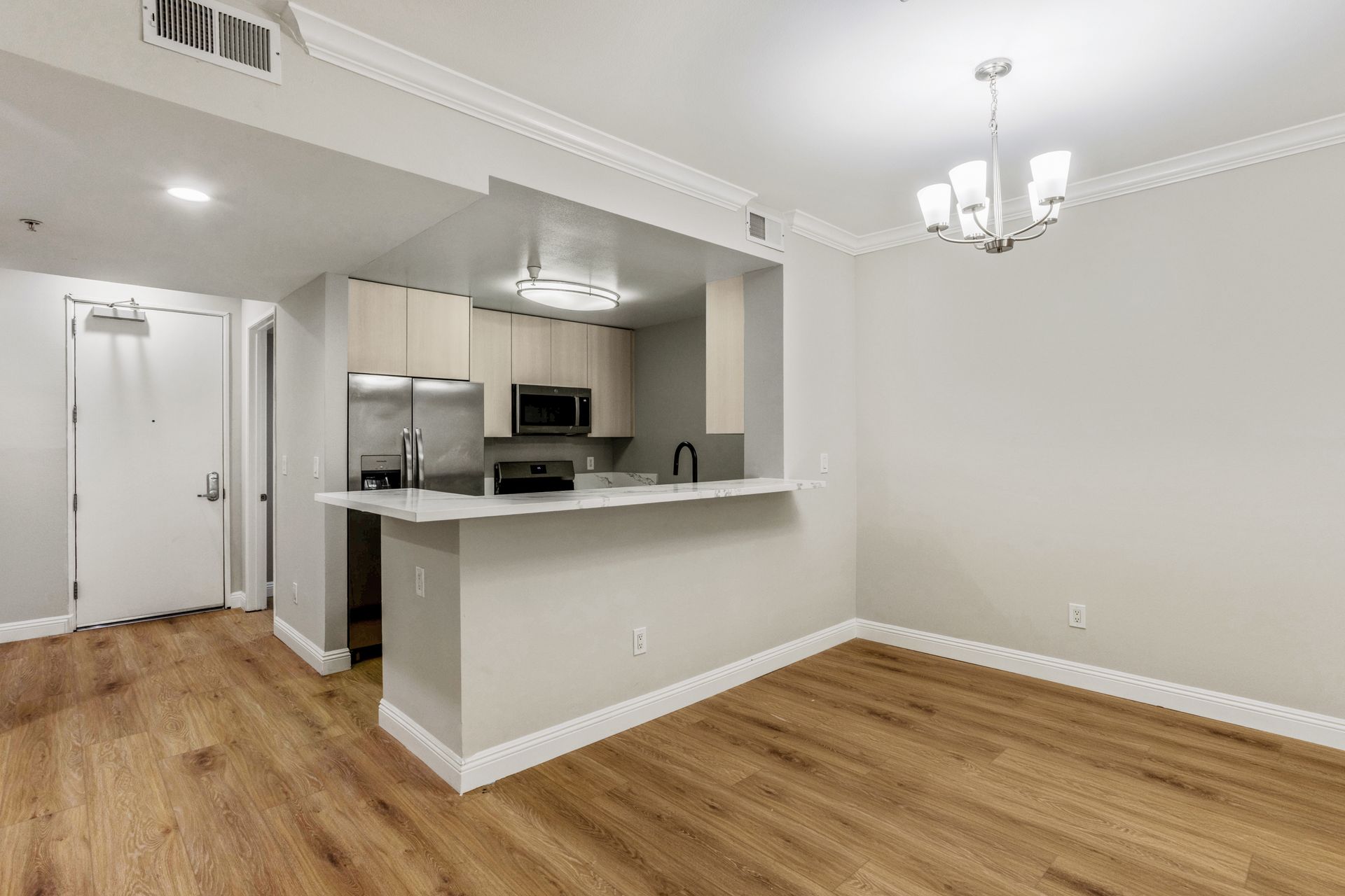 Empty apartment interior with kitchen bar and light wood floors.