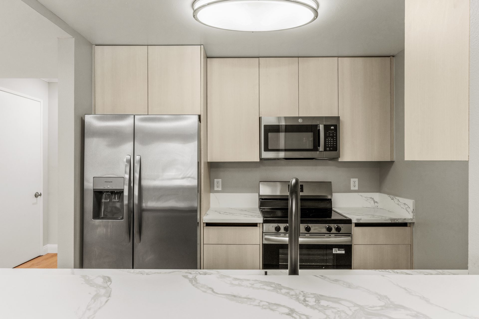 Modern kitchen with stainless steel appliances, light wood cabinets, and marble countertops.