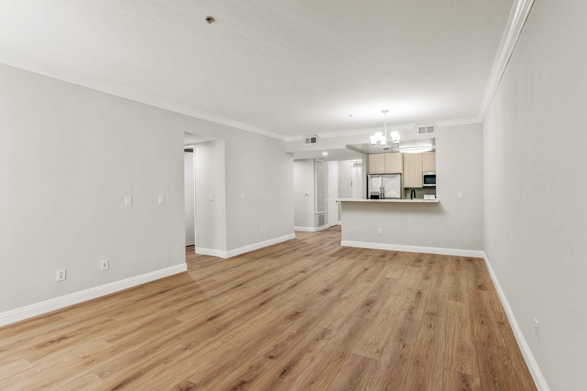 Empty apartment interior, light gray walls, wood-look flooring, open kitchen, neutral tones.
