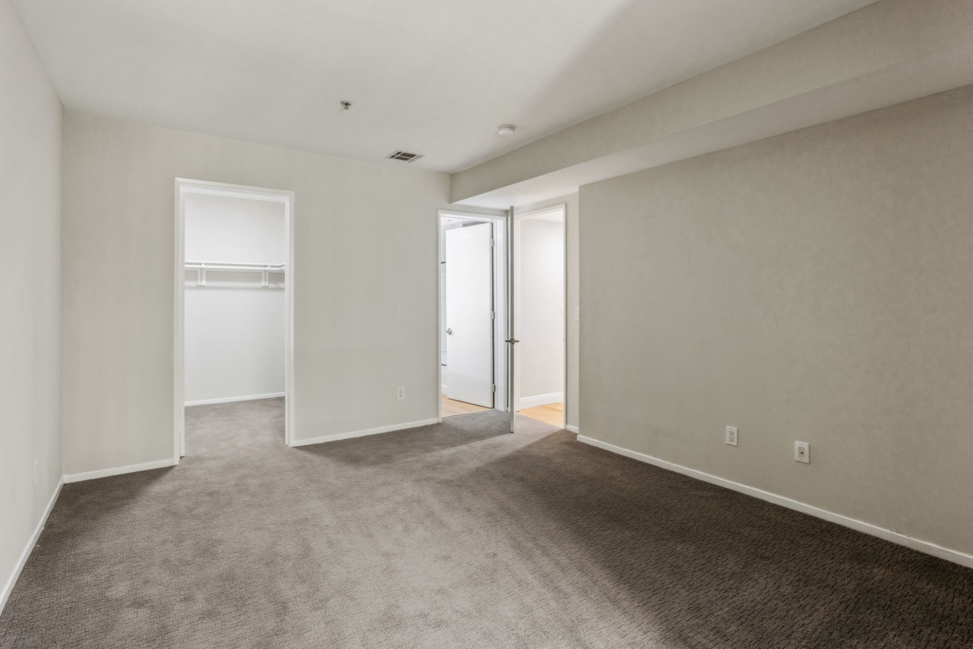 Empty bedroom with gray carpet, walk-in closet, and doorway to bathroom.