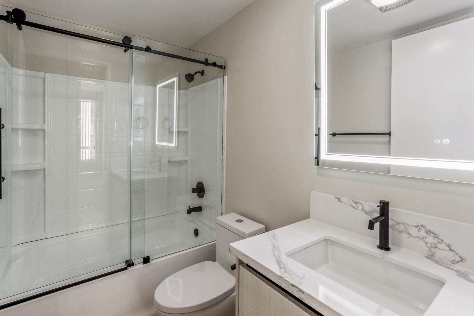 Modern bathroom with a glass shower, white walls, and a marble countertop.