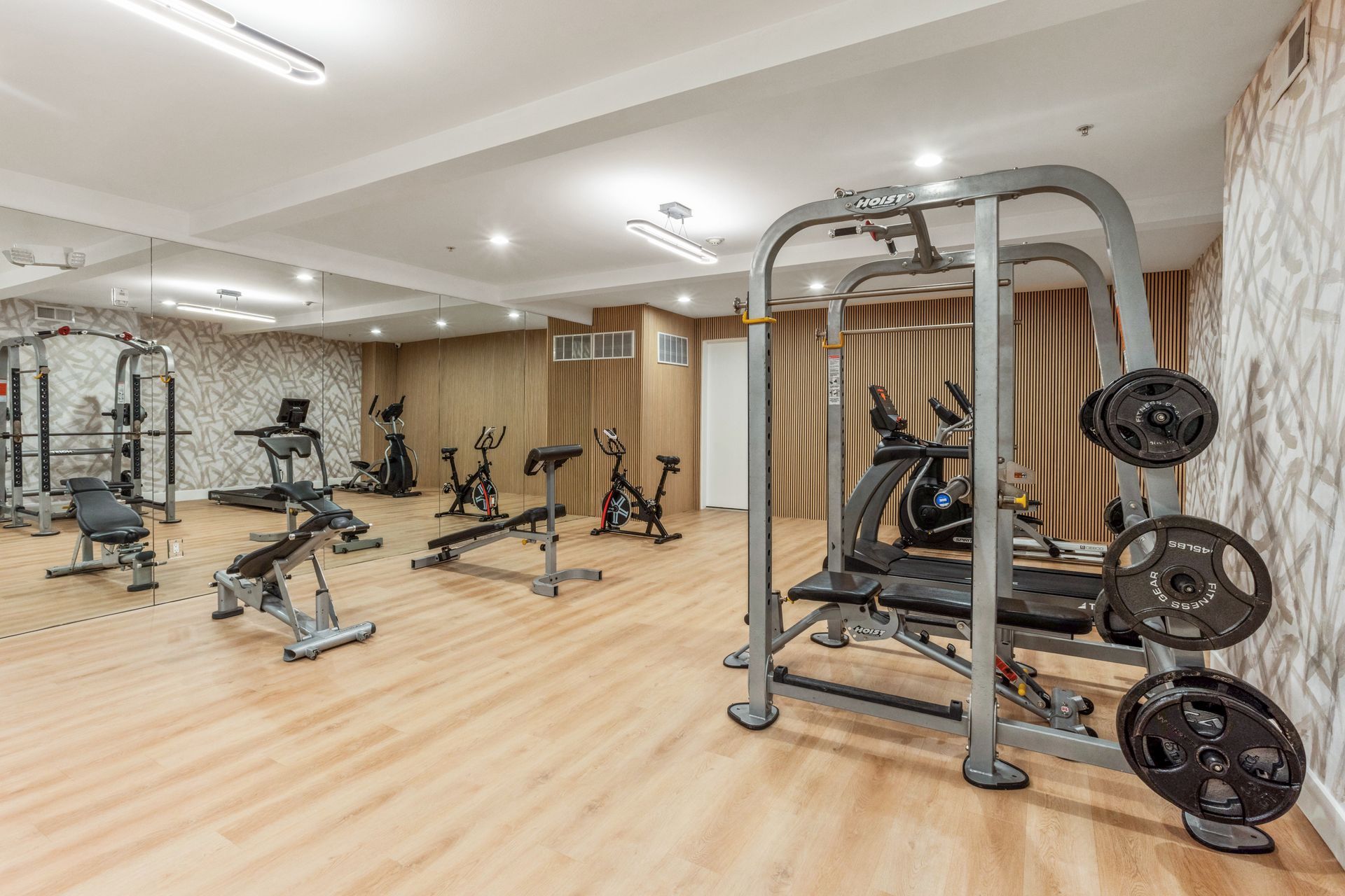Gym with workout equipment on wood flooring, featuring weight rack, exercise bikes, and weight machines.