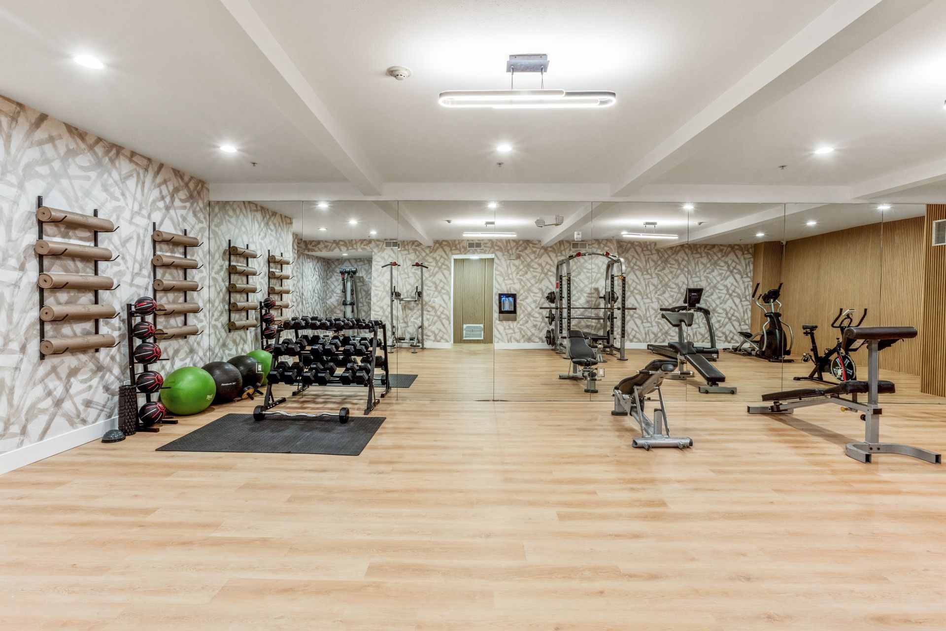 Gym interior with weights, machines, mirrors, and wooden floors.