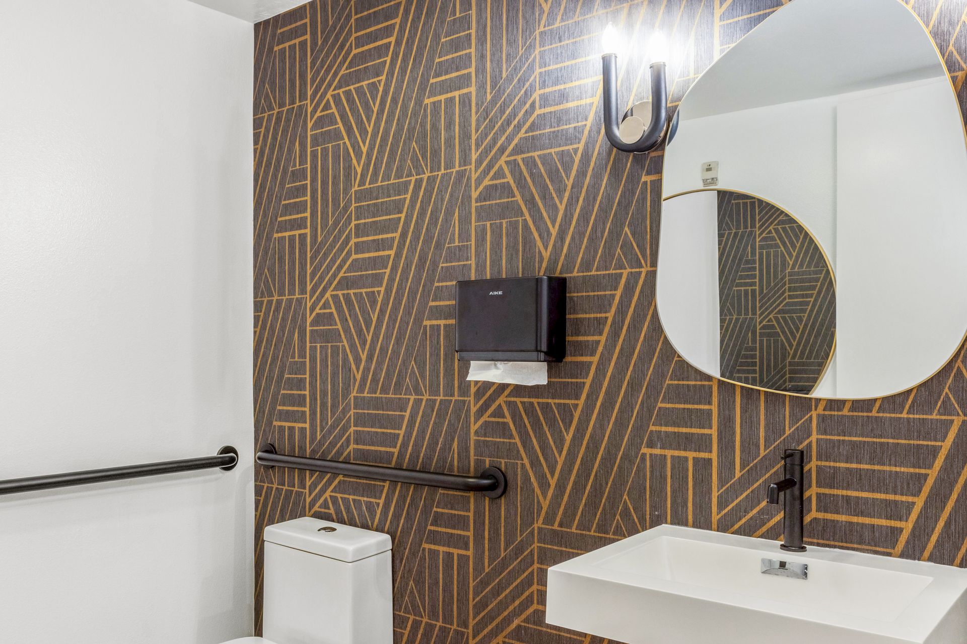 Modern bathroom with geometric patterned wallpaper, white sink, and black fixtures.