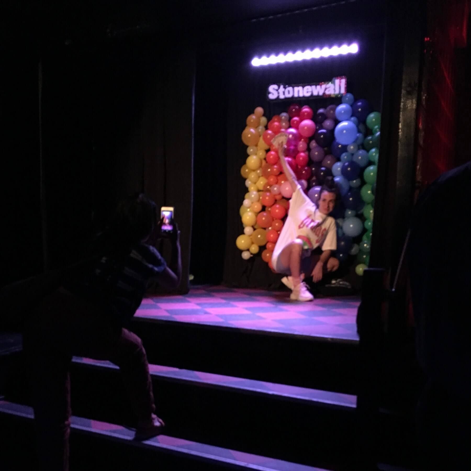 A woman is taking a picture of a man in front of a wall of balloons that says stonewall