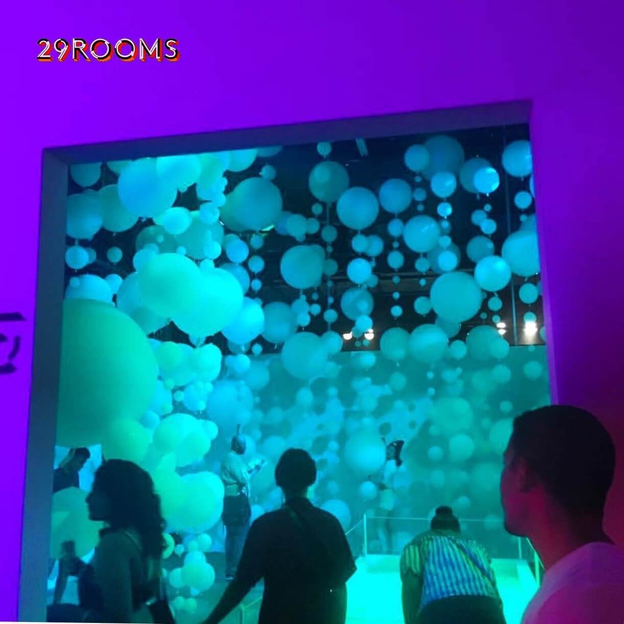 A group of people are standing in front of a screen that says 29rooms