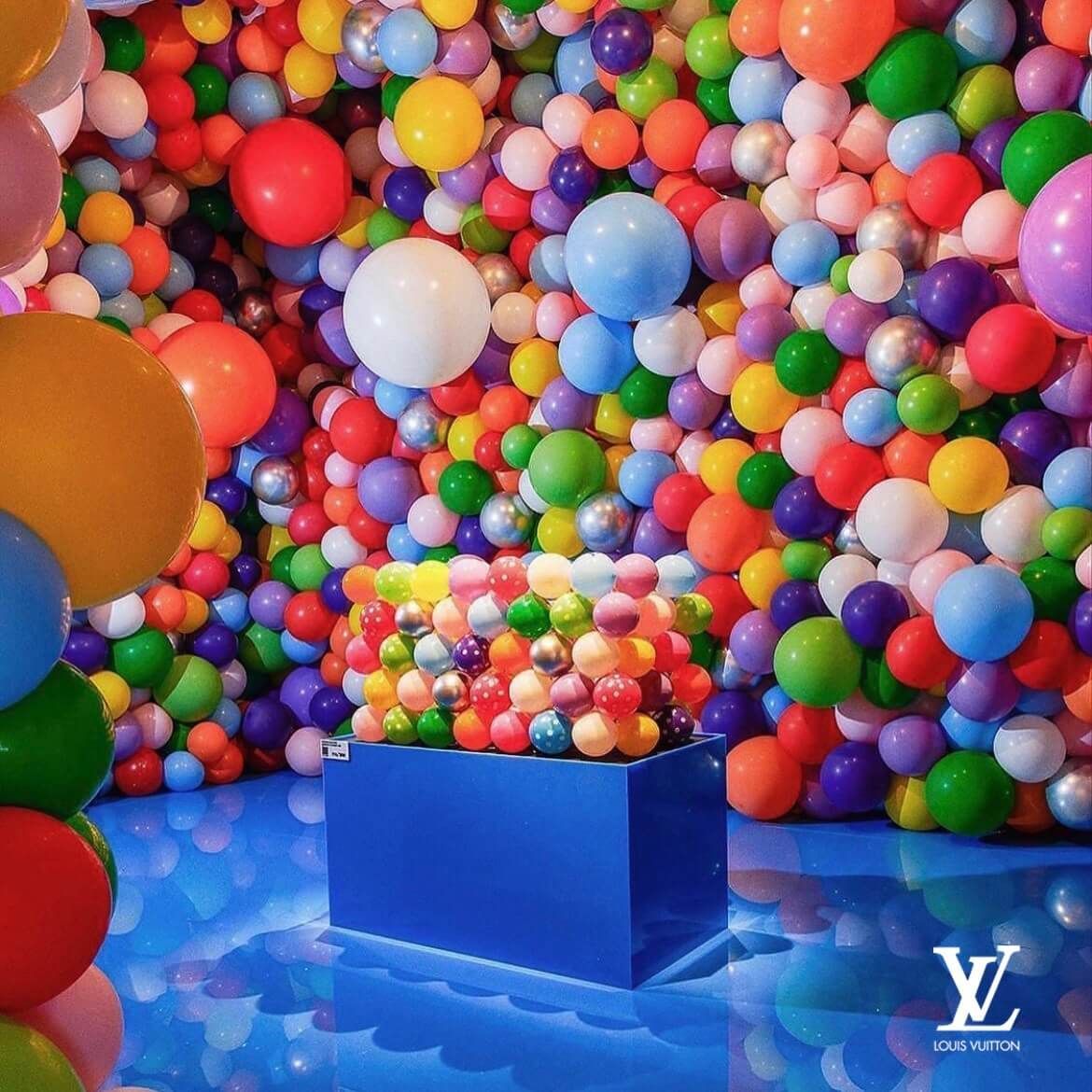A bunch of colorful balloons with a louis vuitton logo in the background