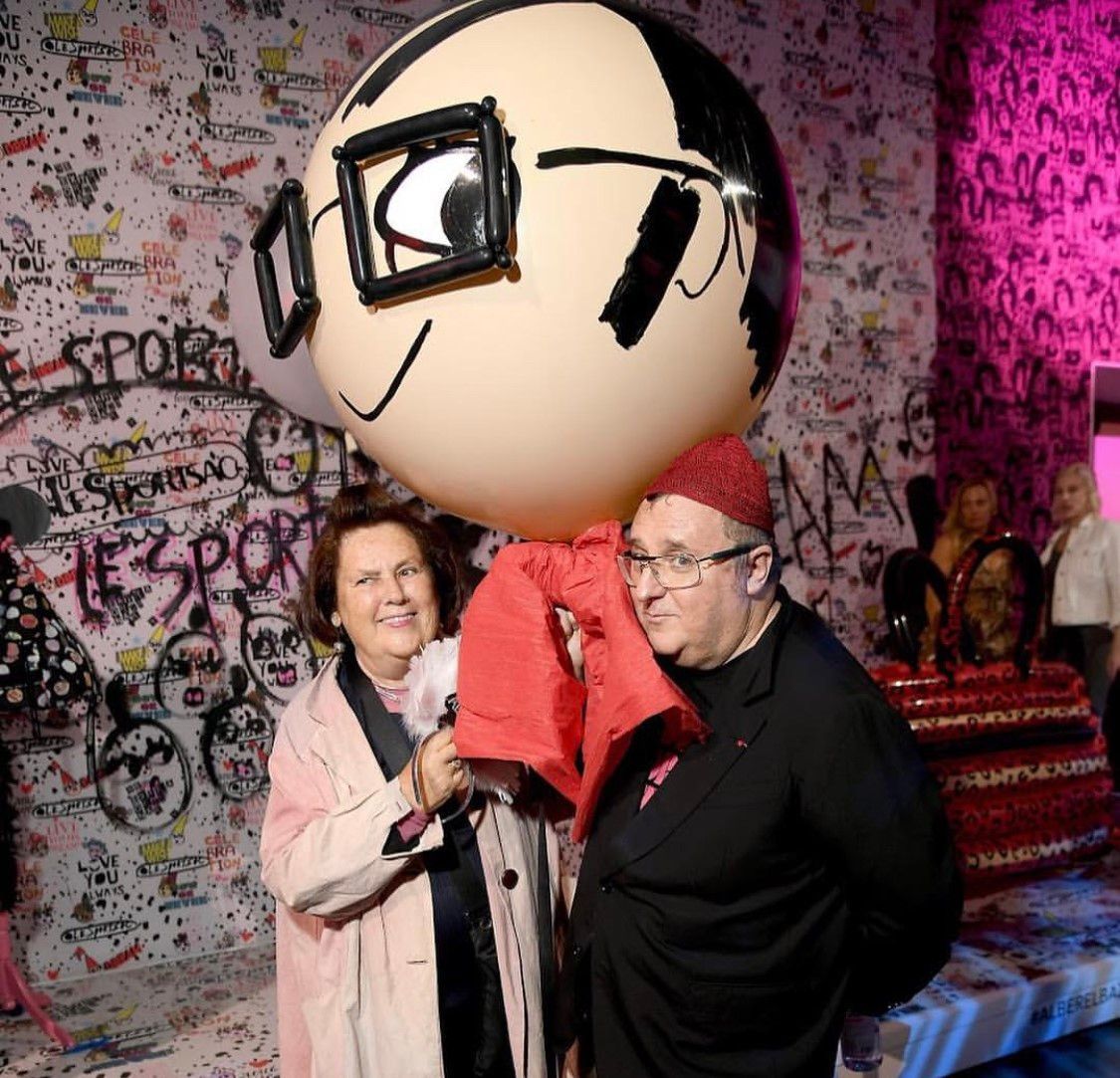 A man and woman standing next to a giant cartoon head with glasses