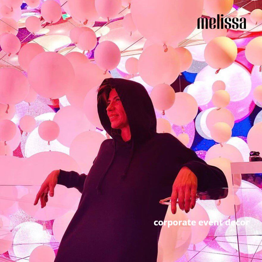 A woman in a black hoodie stands in front of a wall of pink balloons