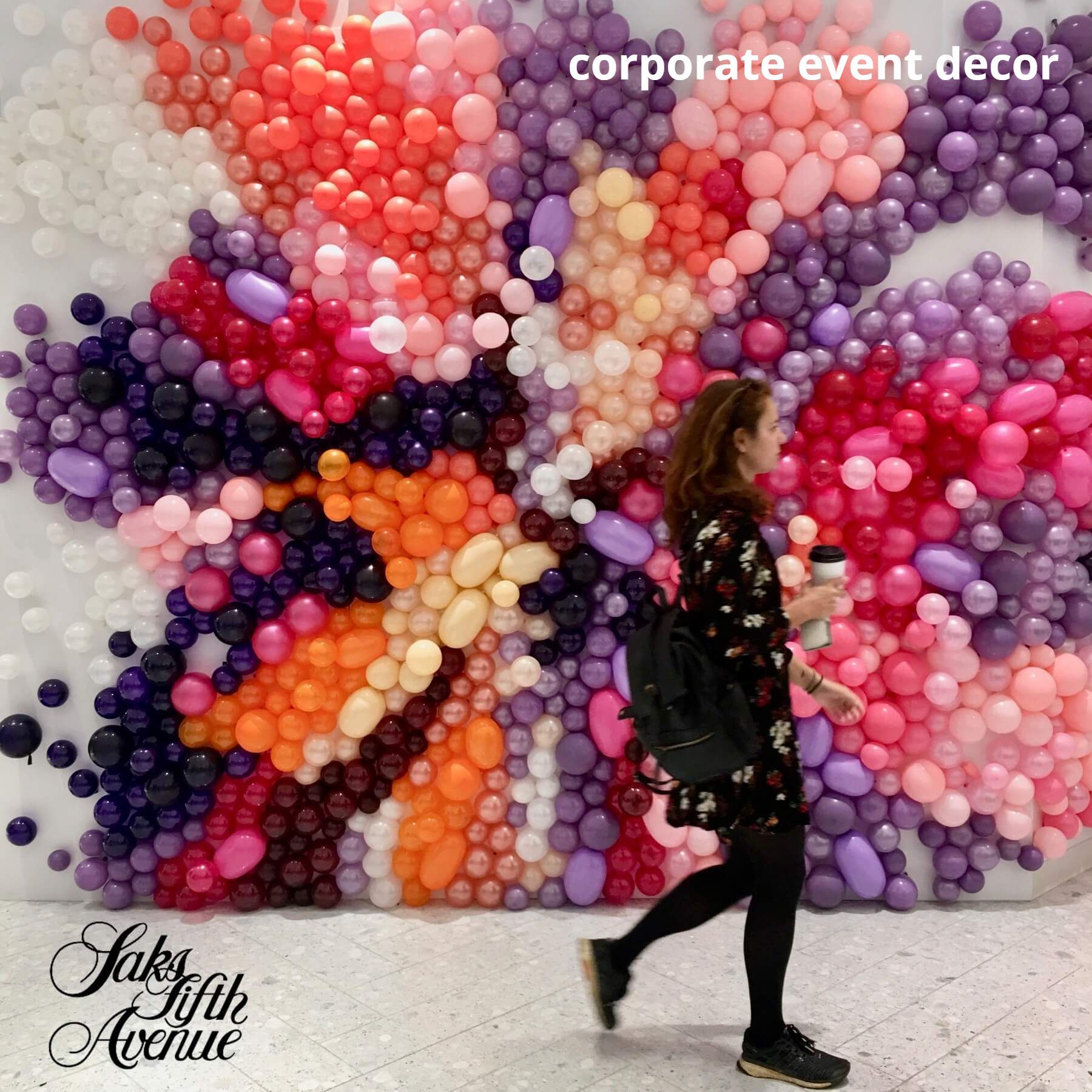 A woman walking in front of a wall made of balloons