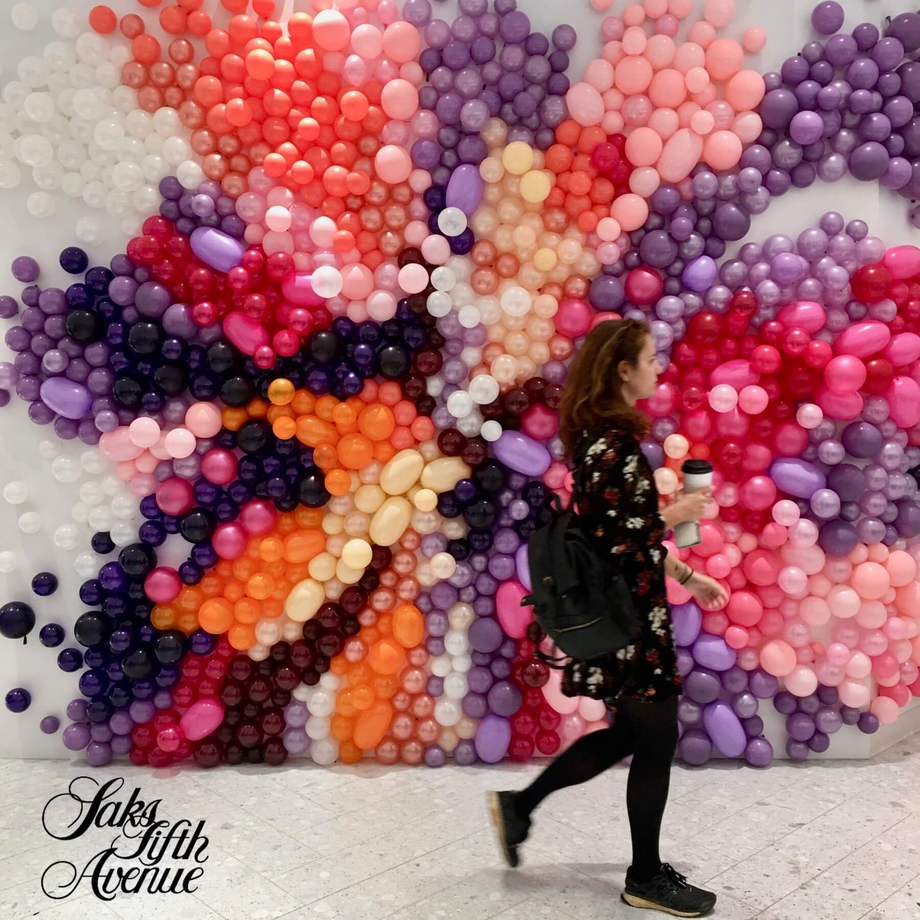 A woman walking in front of a wall made of balloons