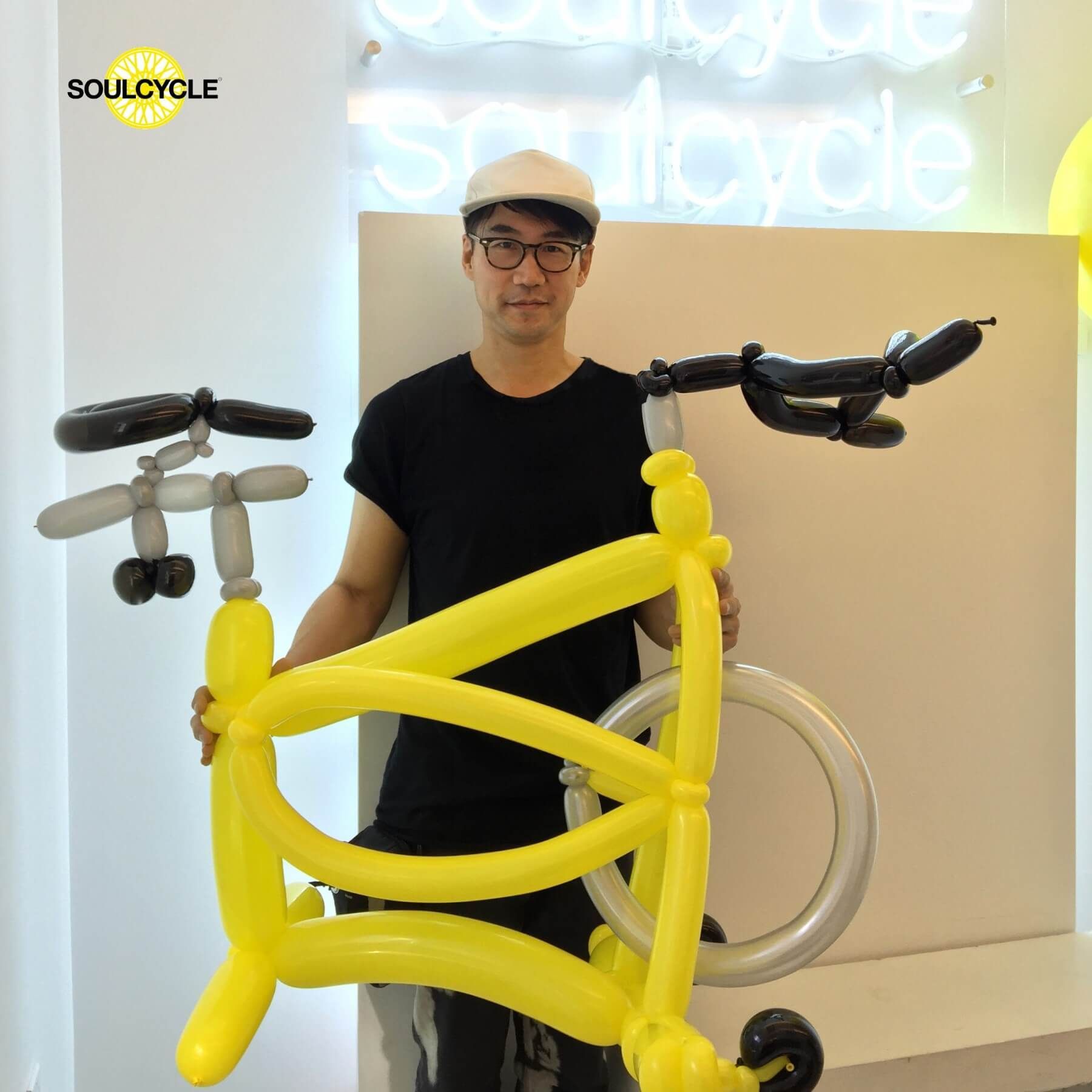 A man is holding a yellow bicycle made out of balloons