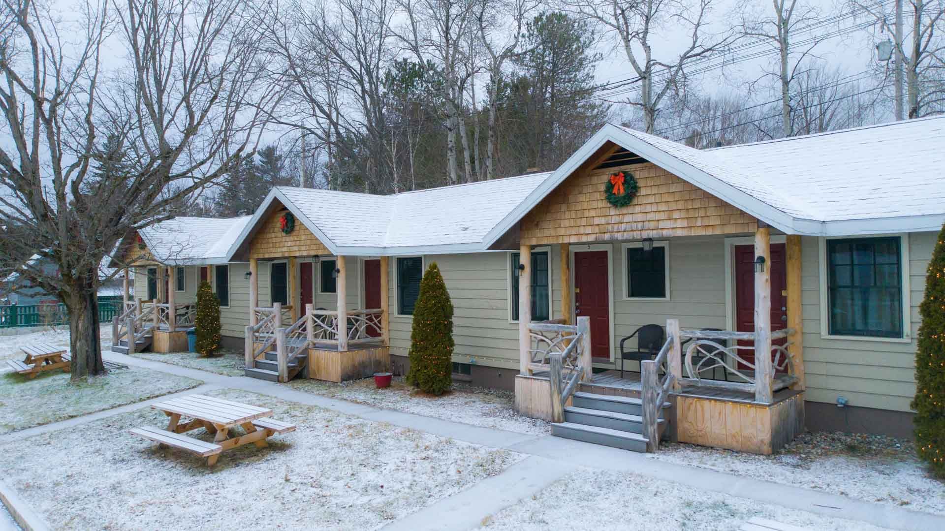 A row of small houses covered in snow with a picnic table in front of them.