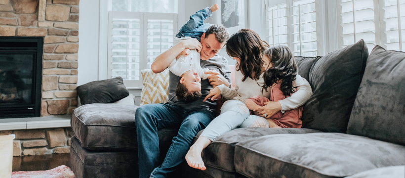 A happy family enjoying time together in their cozy living room with a plush grey sofa and a stone fireplace, exemplifying the comfort and joy of homeownership achievable through VA loan benefits in Spokane.