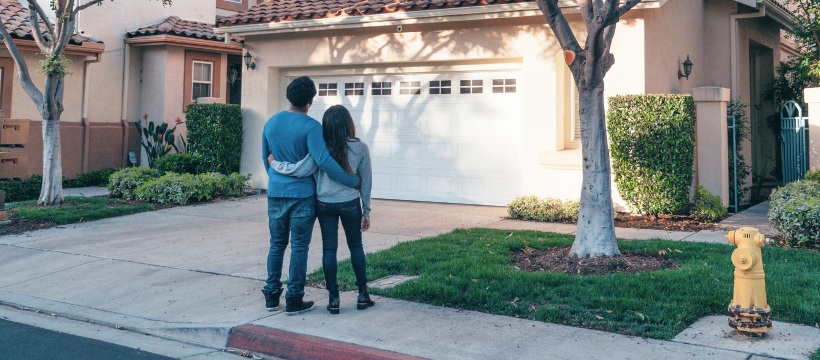 A couple embracing while standing in front of a new home, contemplating the potential of a first-time home buyer loan in Spokane.