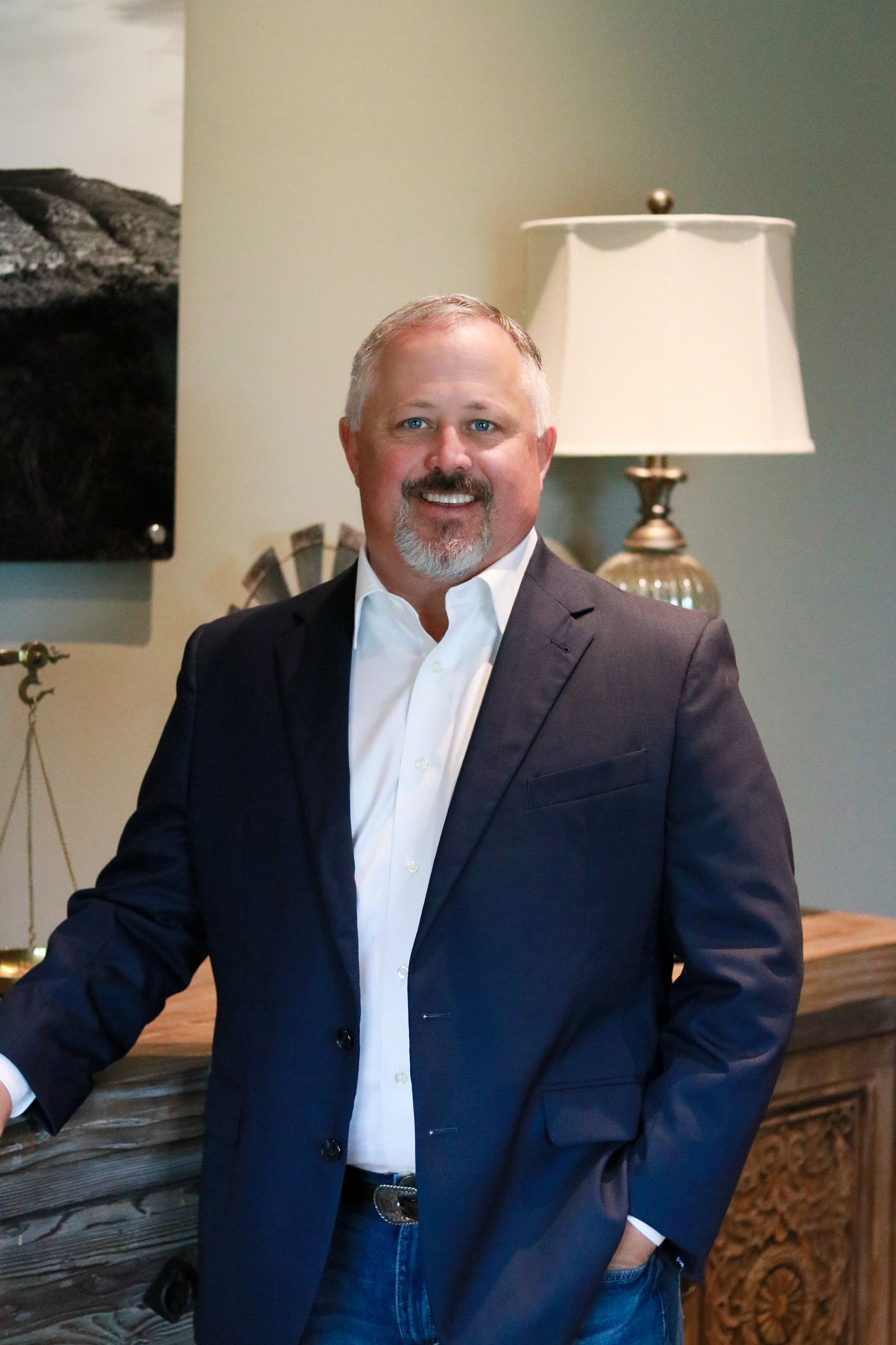 A man in a suit and white shirt is standing in front of a lamp.