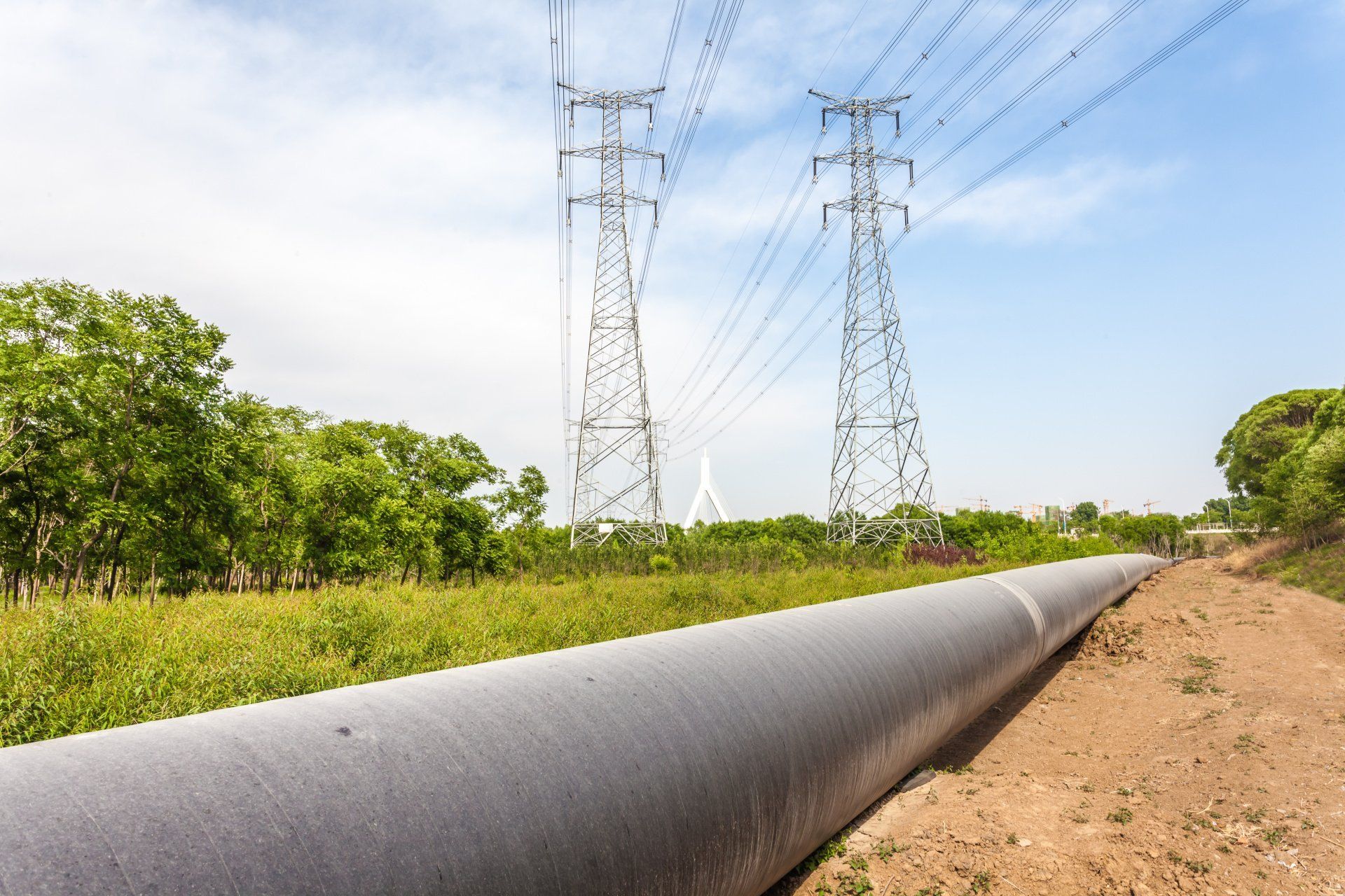 A large pipe is going through a field with power lines in the background.