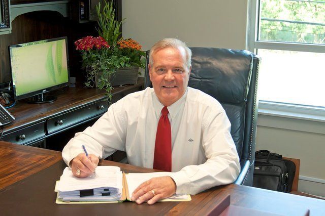 A man in a white shirt and red tie is sitting at a desk.