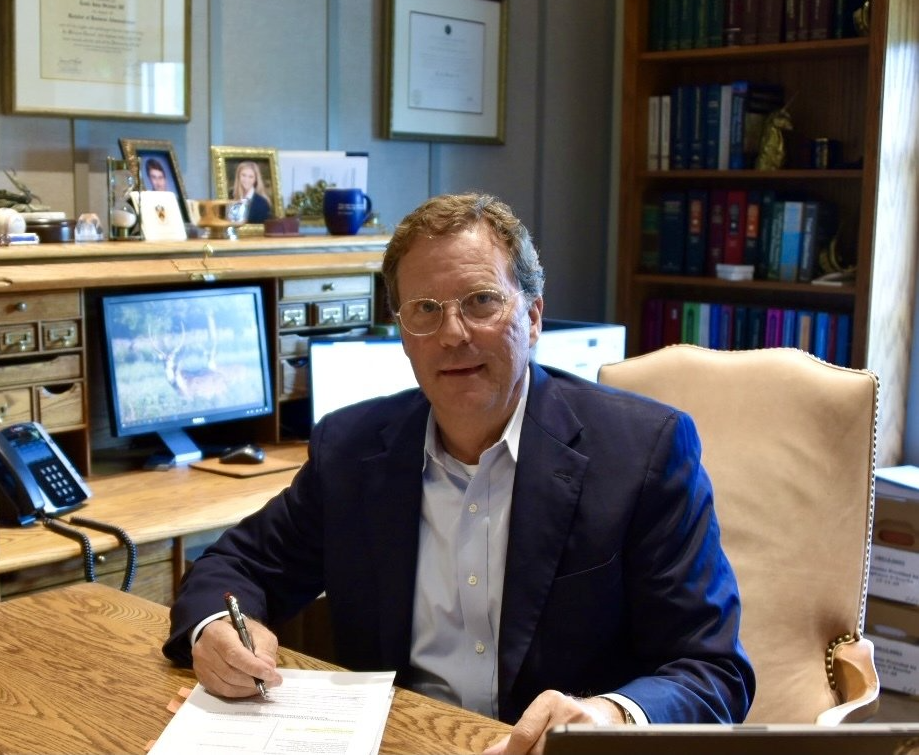 A man in a suit sits at a desk with a laptop