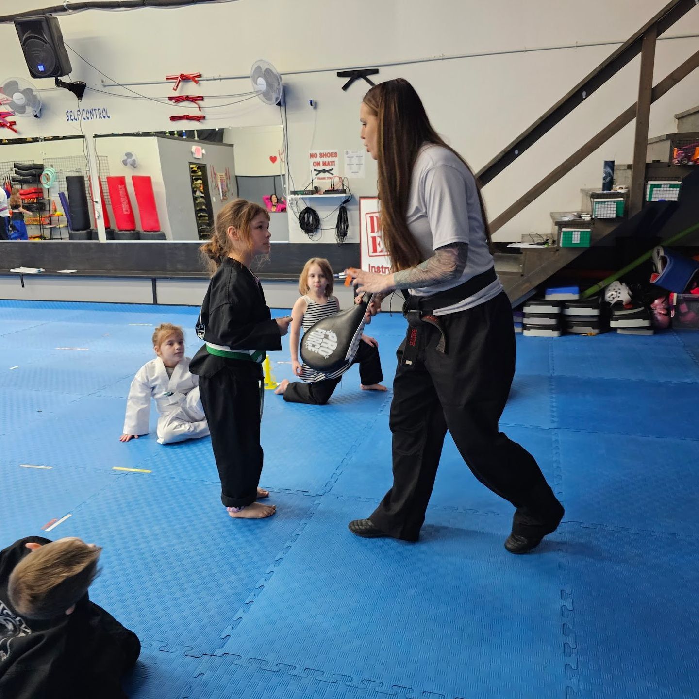 A man is kneeling down next to a young boy in a taekwondo class.
