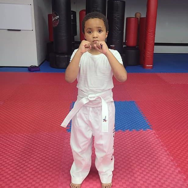 A young girl in a karate uniform is sitting on the floor.
