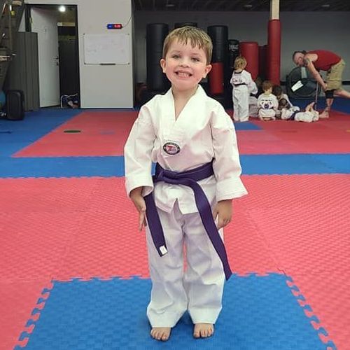 A man is kneeling down next to a young boy in a taekwondo class.